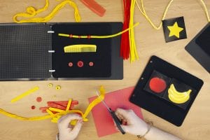 Close up of adult hands cutting red and yellow materials for the APH CVI Book Builder