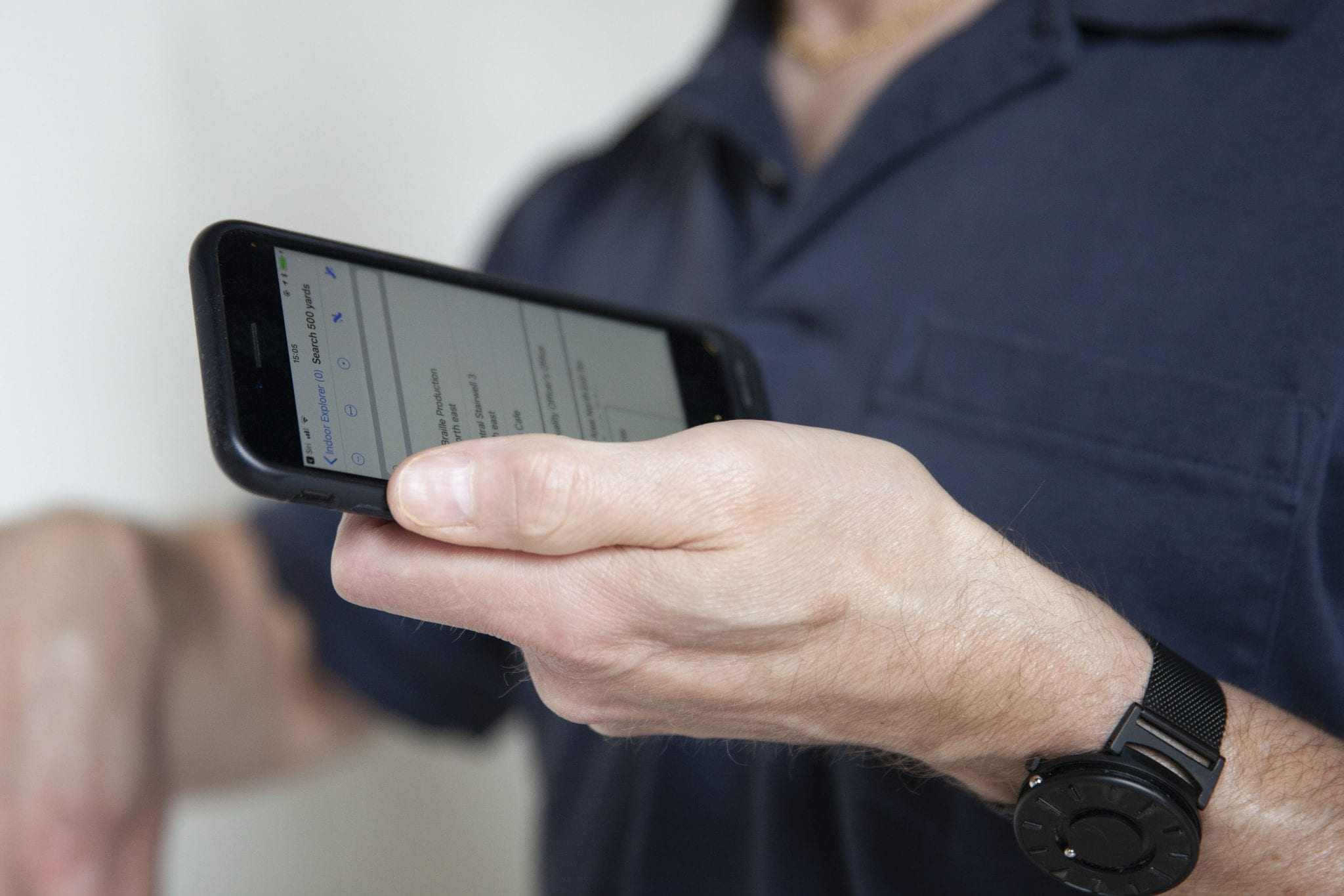 A man’s hand holding an iPhone which is displaying the Indoor Explorer search screen.