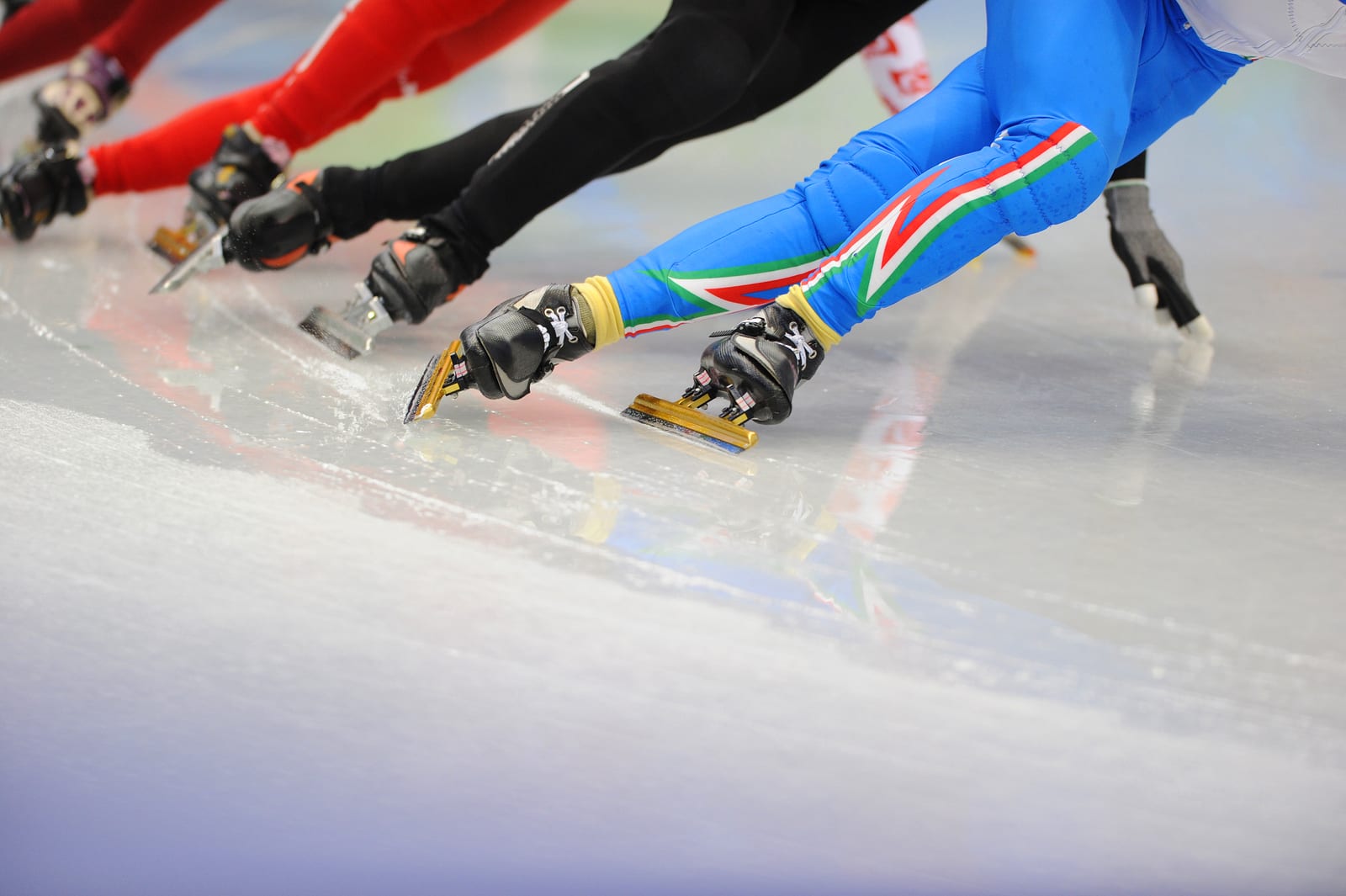 The legs of a group of ice-skaters on the ice.