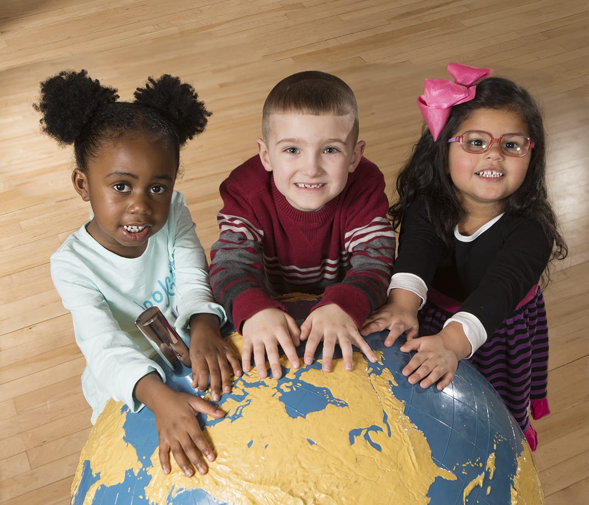 Three smiling children with hands on a large tactile globe