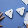 Overhead view of the blue mat with triangle cut-outs and a few blue triangular alphabet tiles. A child's hands are placing a tile into the cut out.