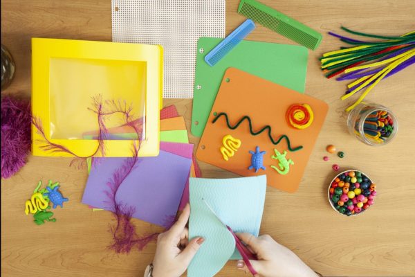 photo shows a pair of hands cutting blue paper over a table containing parts from the Tactile and CVI Book Builder kits