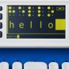 SMART Brailler with a black screen and lime green text that reads “Hello” in simbraille at top and large print then small print at bottom.