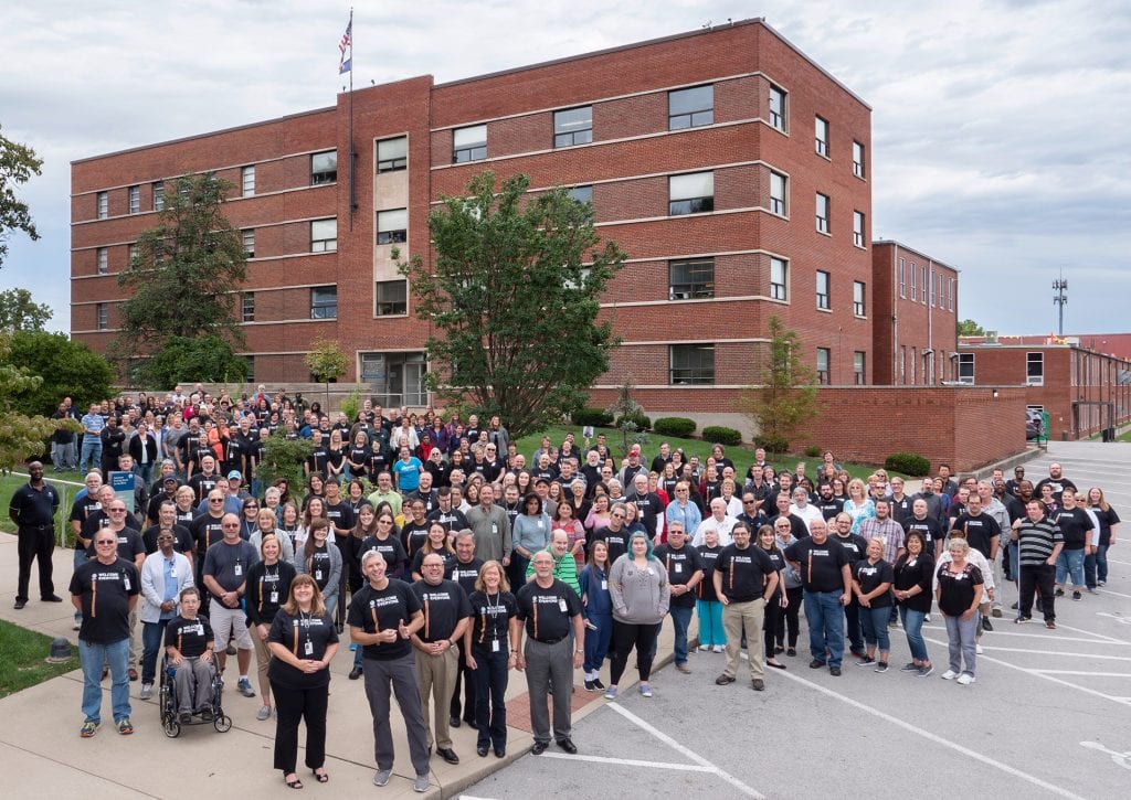 the staff of APH standing on the front lawn smiling with the building behind them