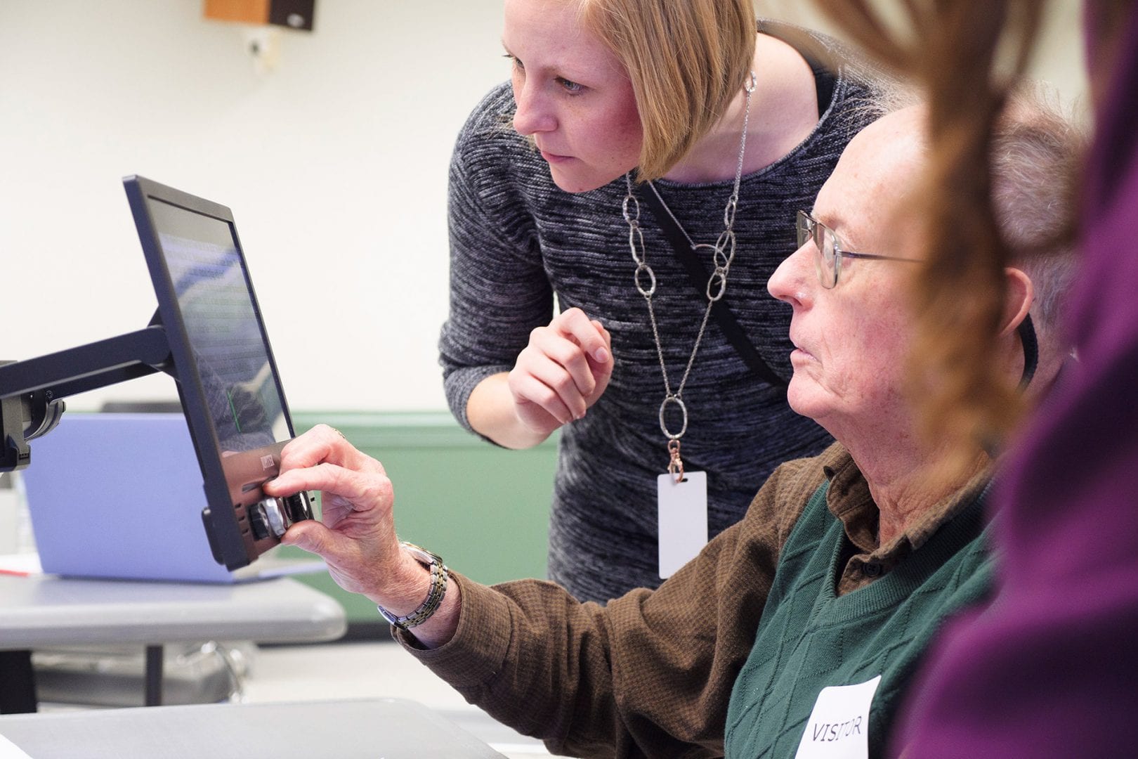 a woman helping a man use the APH Jupiter to magnify a document