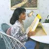 A woman sitting at a table using the GrandStand Portable Reading Easel