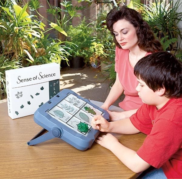 A woman and a boy seated at a table using Sense of Science: Plants overlays with a light box