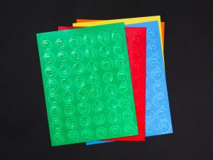 A stack of Smiley-Frowny Feel 'n Peel Sticker sheets in a variety of colors laid out on a black background.
