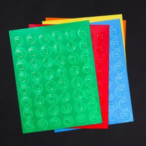 A stack of Smiley-Frowny Feel 'n Peel Sticker sheets in a variety of colors laid out on a black background.