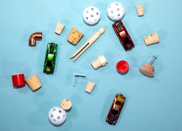 All the components of Pack A (wiffle balls, pins, corks, small toy cars) strewn out on a blue background.