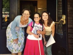 Jess in elementary school with her white cane and her teacher standing to her left