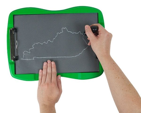 A tactile graphic in the shape of Kentucky drawn on tactile drawing film is attached to the green TactileDoodle frame. Two hands are in the photo; one is holding the film in place, and the other is tracing the outline of the Commonwealth