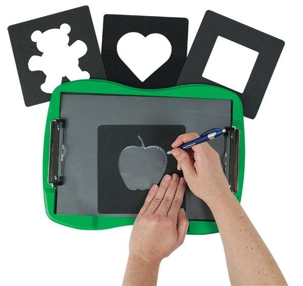 Two hands are tracing the inside of an apple shaped stencil on tactile drawing film attached to the TactileDoodle. Three additional stencils are laid out above the TactileDoodle. From left to right, there is a teddy bear, a heart, and a square.