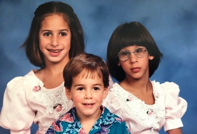 a vintage portrait photo from the late 80s or early 90s of a three children. An older sister, Rachel the middle child in glasses, and a younger brother.