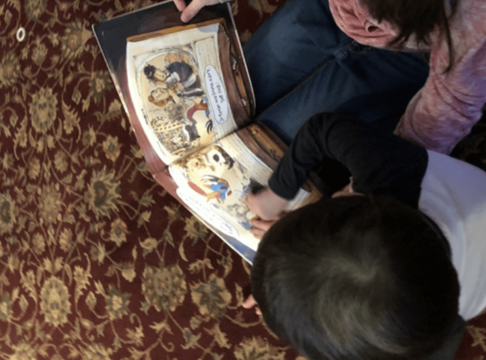 overhead shot of an older girl helping a younger boy read a braille story book
