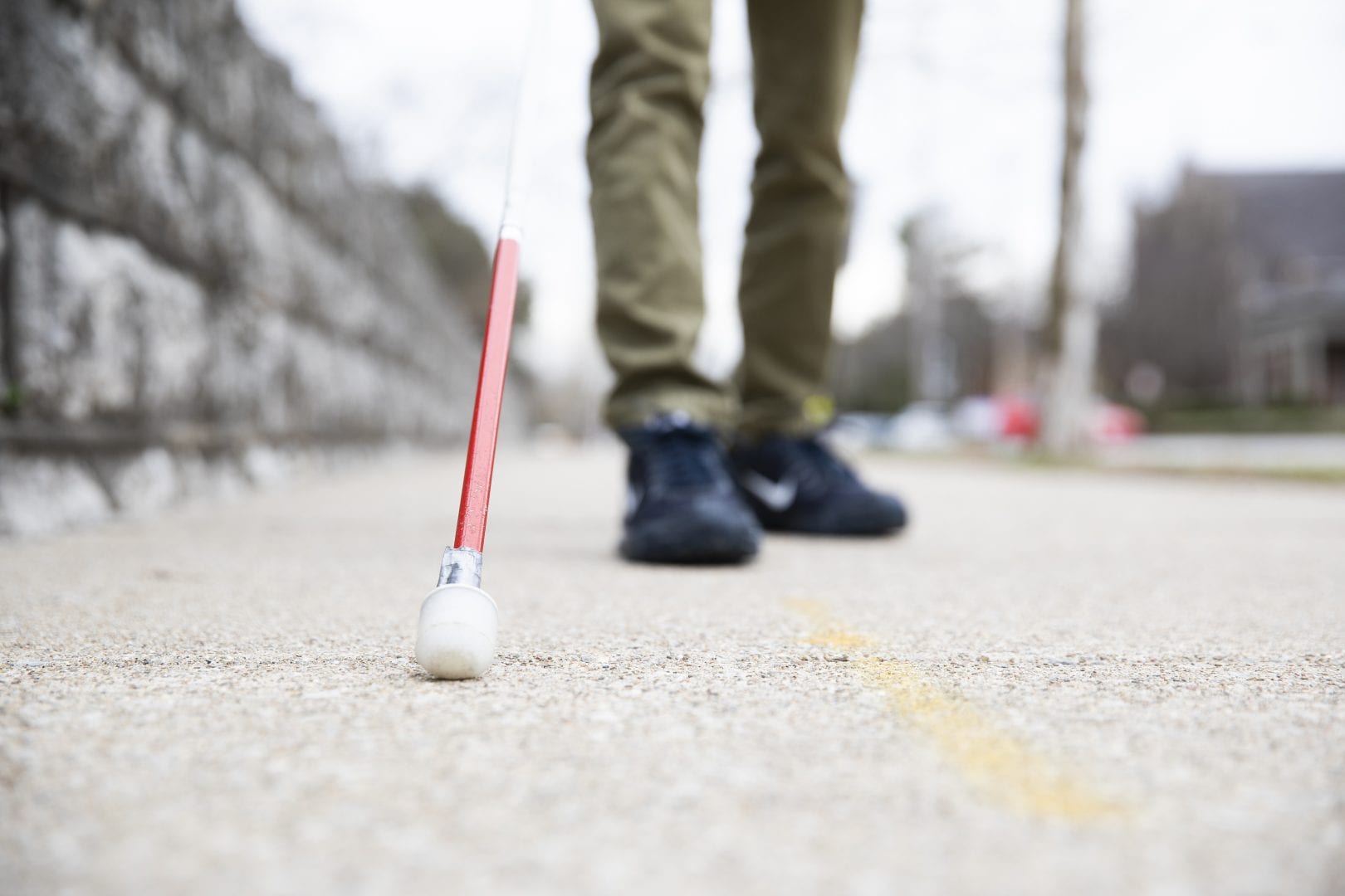 close up of a white cane with a red tip on concrete, sneakers in the background