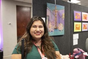 photo of a young woman holding smiling and standing in front of her artwork