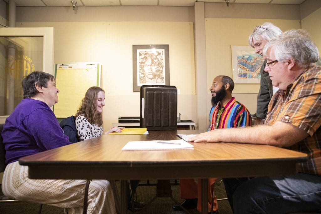 Actors sit around a table going over their lines