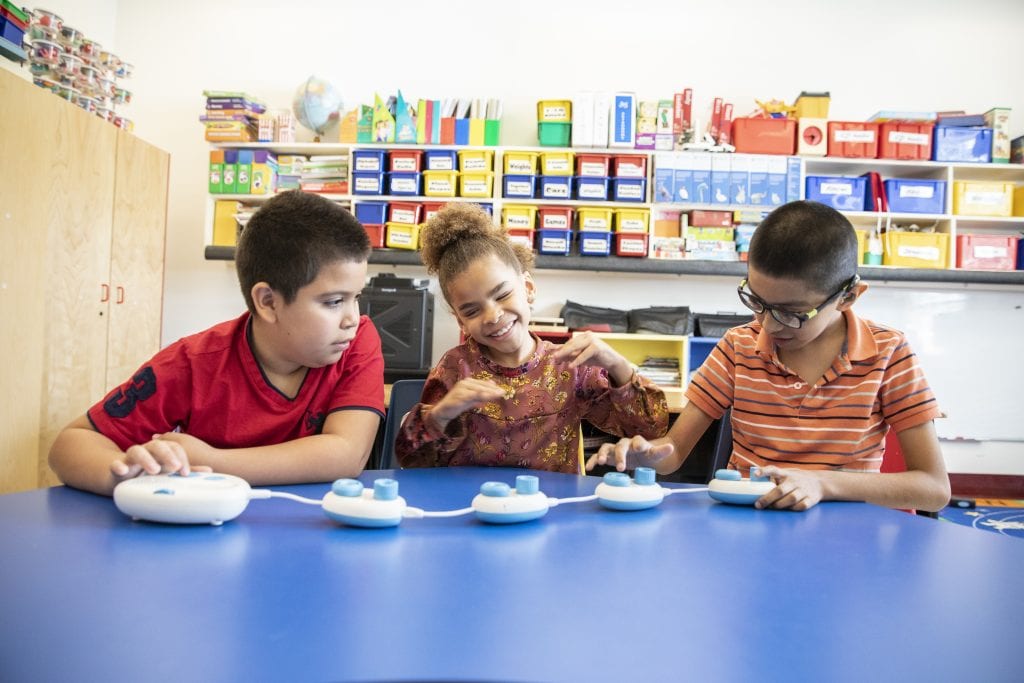 three students in a classroom smiling and playing with code jumper