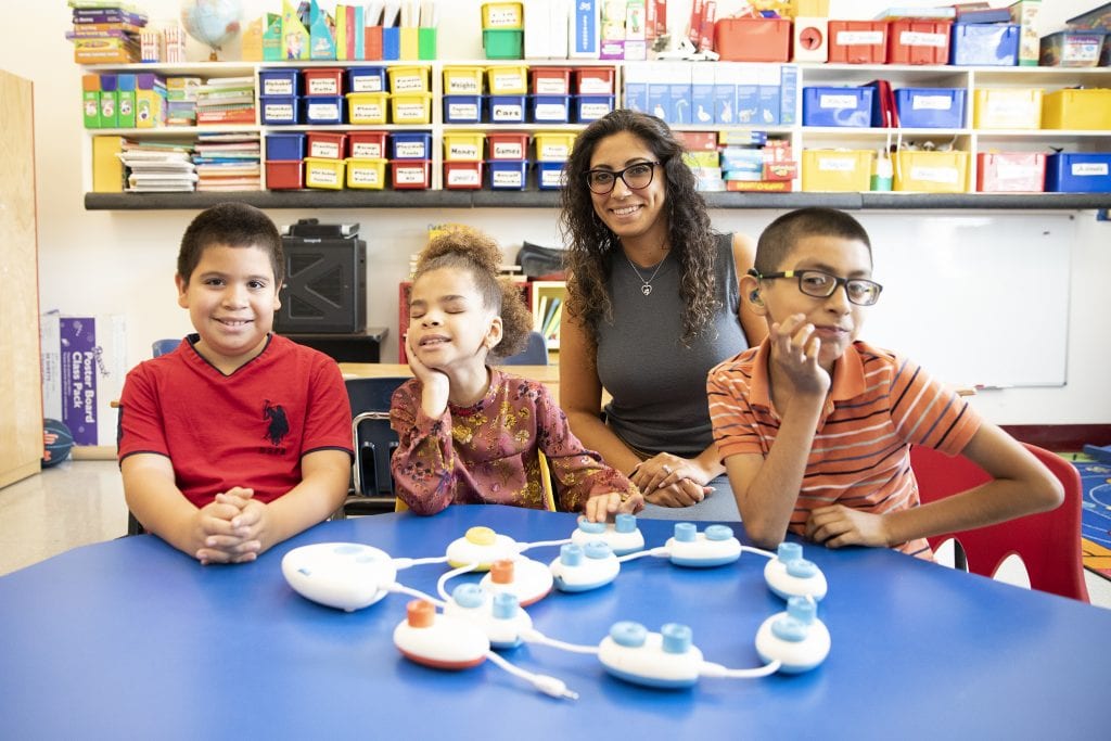 three students and a teacher posing for the camera in a classroom code jumper on the table in front of them