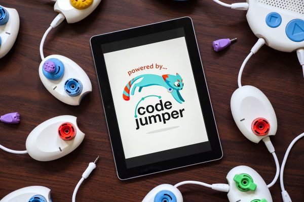 A tablet sitting on a table displaying the Code Jumper logo. Code Jumper pods lay on the table surrounding the tablet.