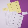 Two stacks of print-braille syllable card sheets, one yellow and one white. Next to each stack is one card that has been punched out.