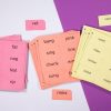 Three stacks of perforated print-braille word card sheets in red, orange, and yellow against a white and purple background.