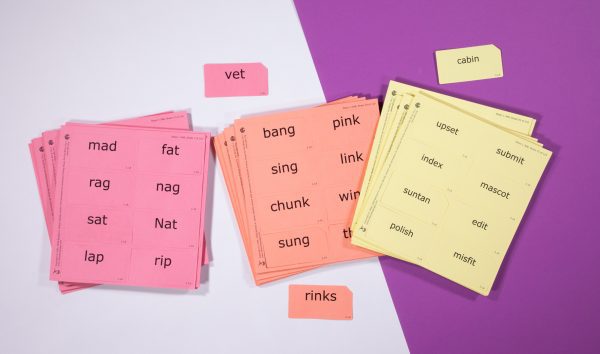 Three stacks of perforated print-braille word card sheets in red, orange, and yellow against a white and purple background.