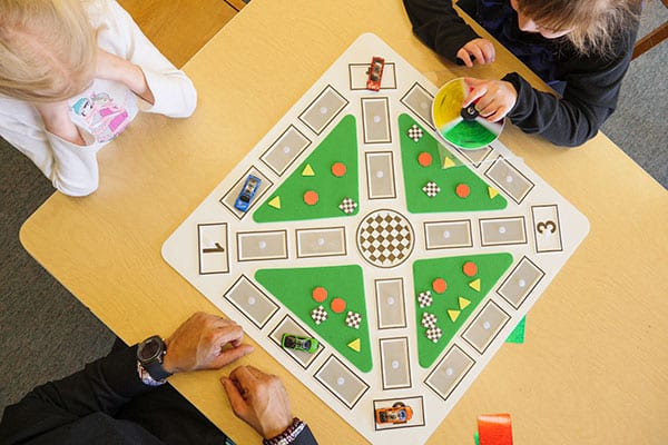 overhead view of two students and an adult sitting around a color raceway board playing the game