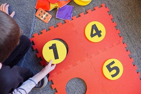 a student placing a foam yellow dot with the number one on it into the red foam floor mat braille cell