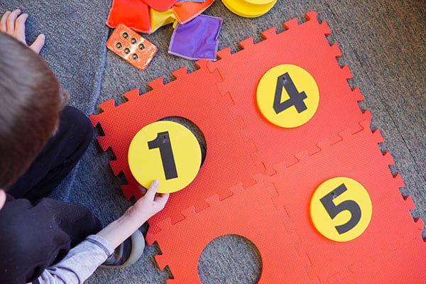 a student placing a foam yellow dot with the number one on it into the red foam floor mat braille cell
