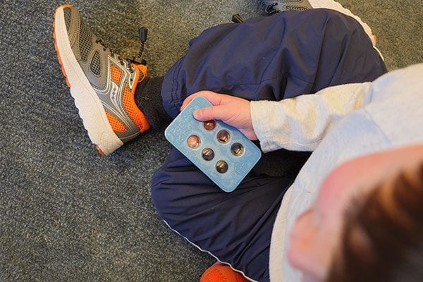 child holding a blue pop-a-cell block with braille on it