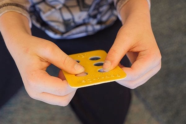 child holding a yellow pop-a-cell block with braille on it