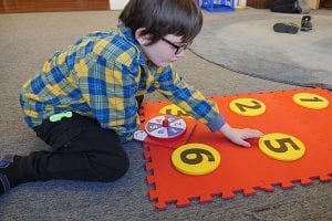 A student placing a foam yellow dot with the number five on it into the red foam floor mat braille cell.