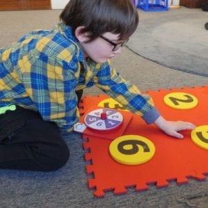 A student placing a foam yellow dot with the number five on it into the red foam floor mat braille cell.