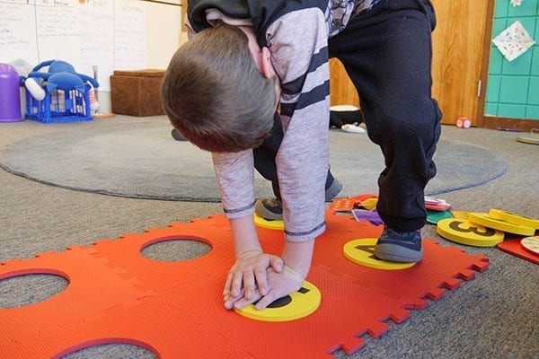 A student placing a foam yellow dot with the number five on it into the orange foam floor mat braille cell.