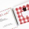 An open storybook. On the left page it says "Let's eat!" in big red font. On the right page there is a red gingham background. A white pocket in the center holds a little felt figure of wolf with a red tongue.