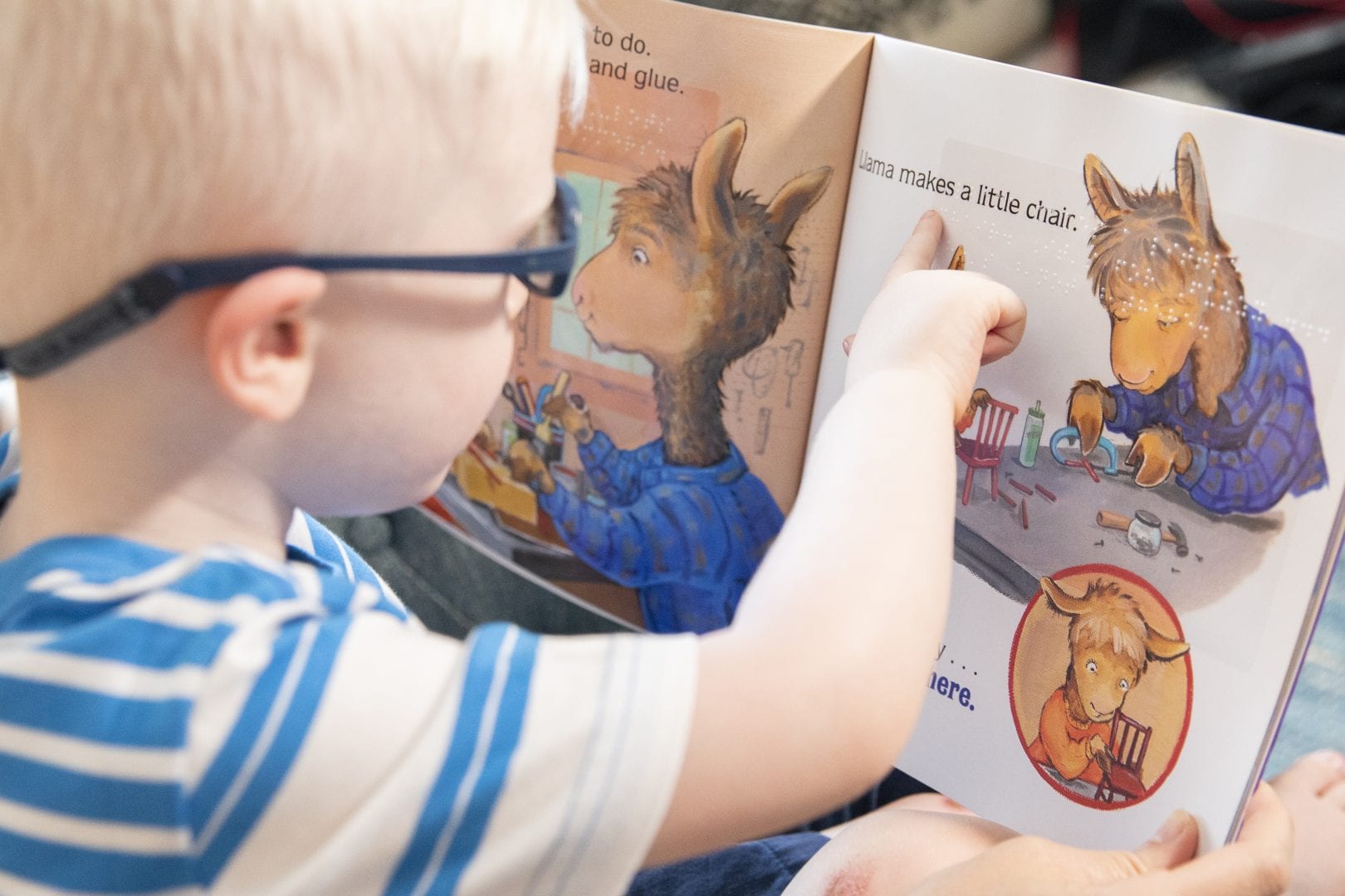 a young boy in glasses touching the braille in a Llama Llama book