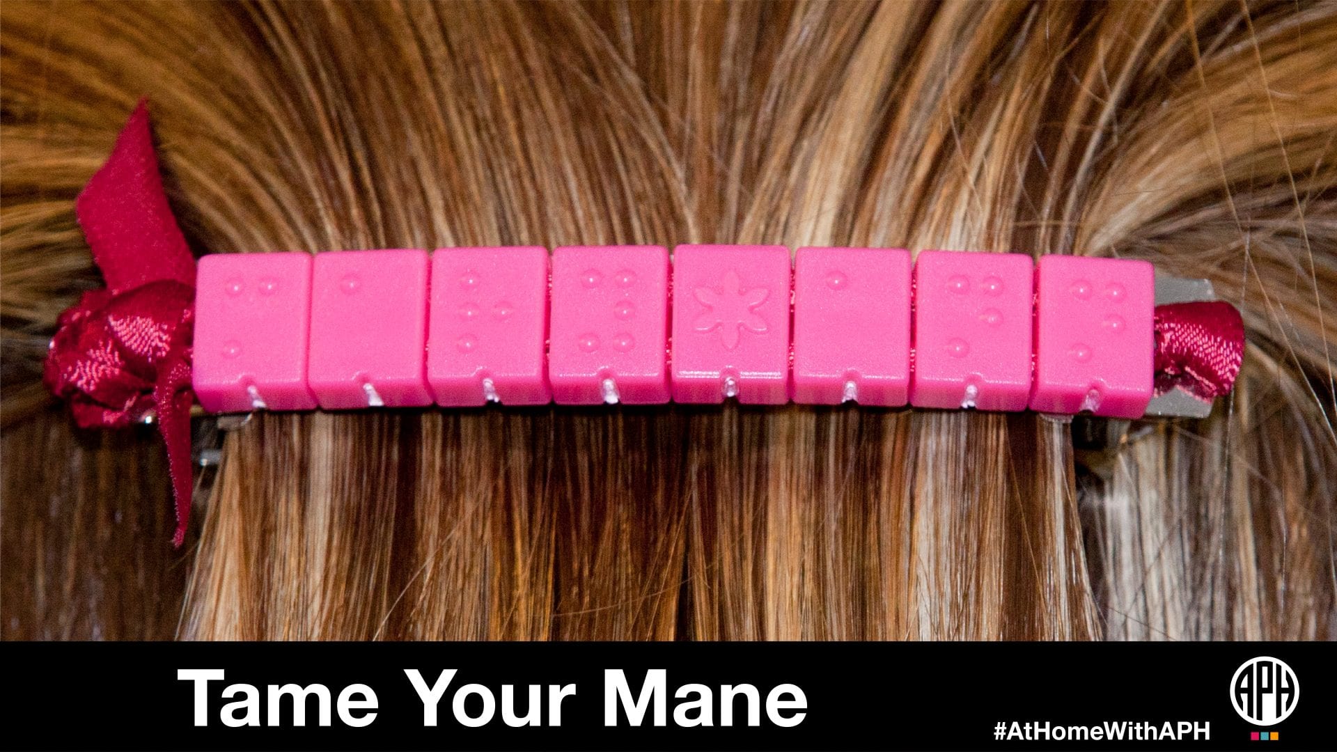 a barrette made of pink braille beads in hair. text reads "tame your mane #AtHomeWithAPH"