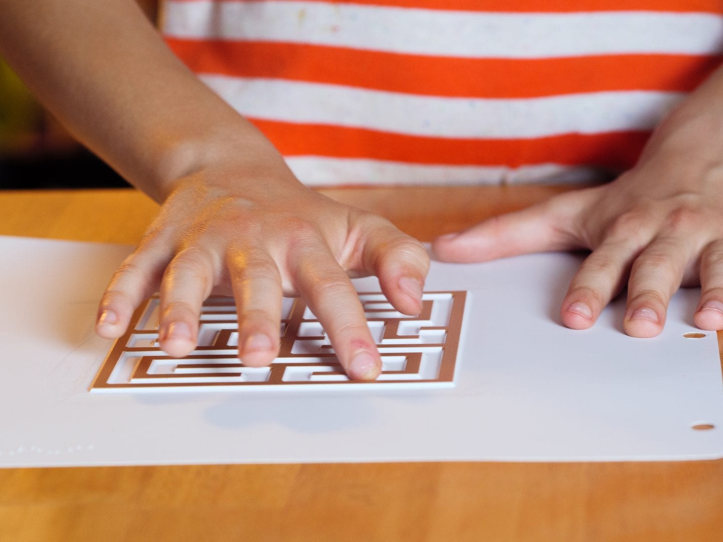 A child standing at a table with one of their hands exploring a Finger Walks tactile labyrinth.