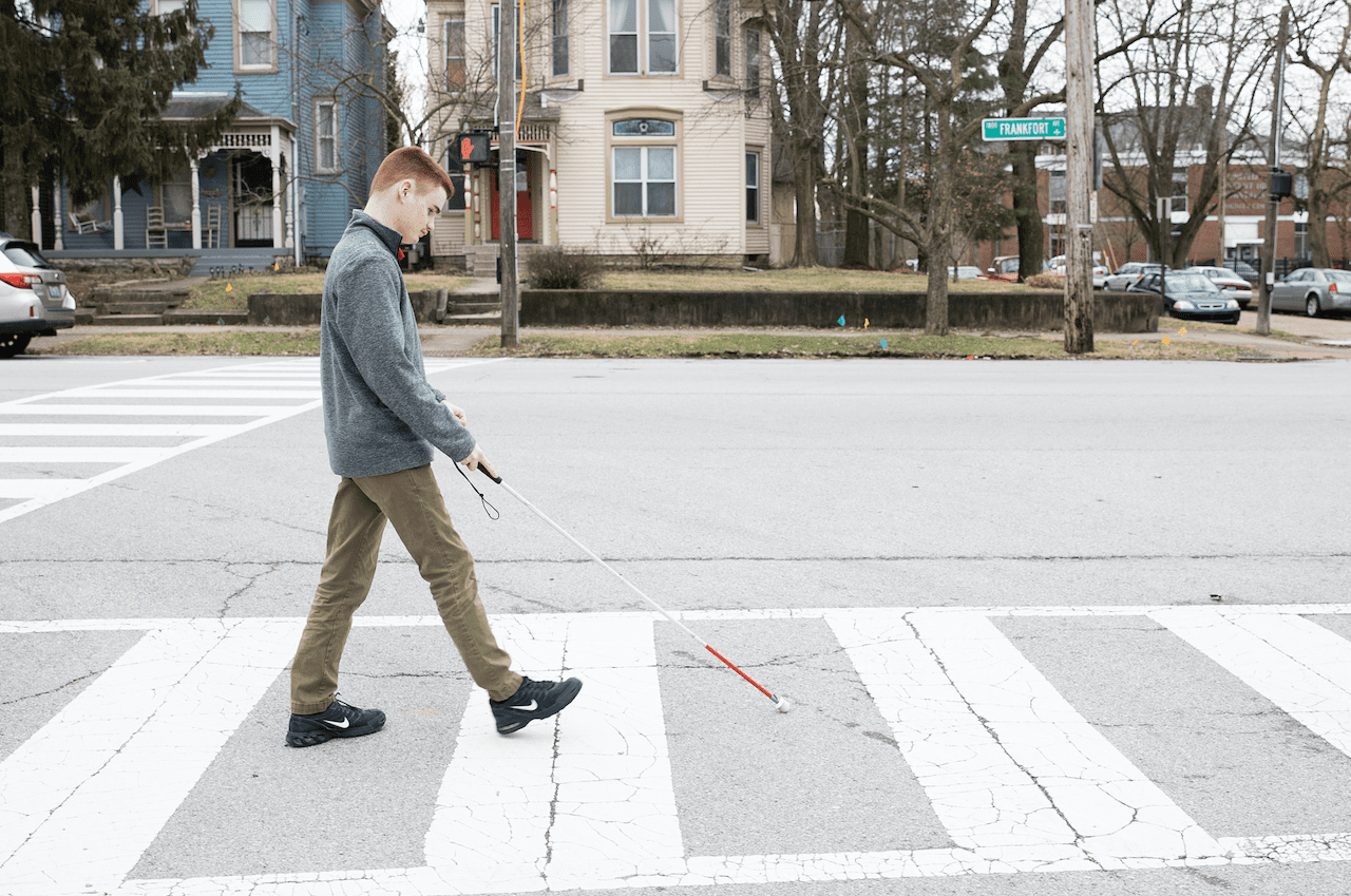 a teenage boy walking across the street at a crosswalk with a white cane