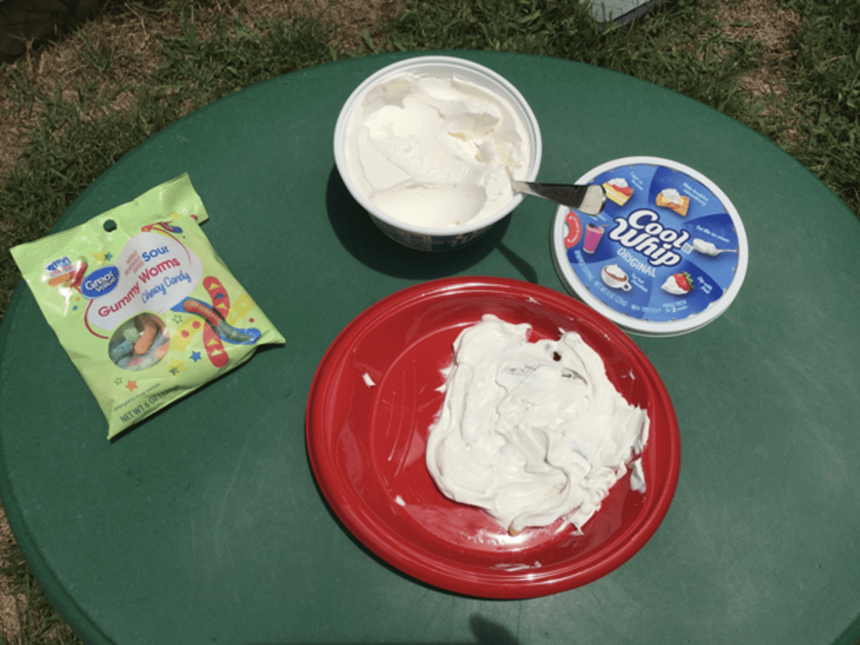 a bag of gummy worms, a container of cool whip, and a plate with cool whip on it sitting on the table