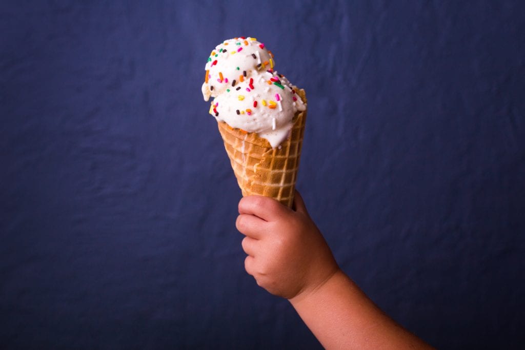 A child's hand holding an ice cream cone with two large scoops of ice cream on it.