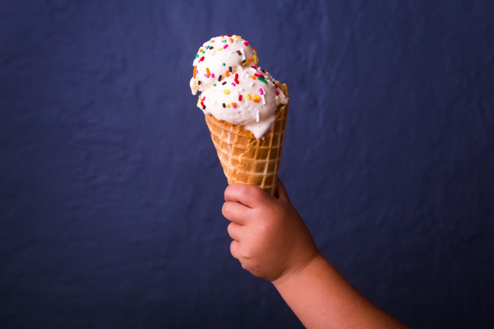 A child's hand holding an ice cream cone with two large scoops of ice cream on it.