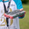 kid holding a gray braille display with a braille keyboard and pink bumper case