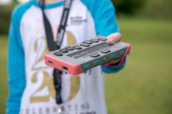 kid holding a gray braille display with a braille keyboard and pink bumper case