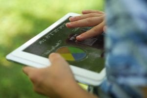 A child outside holding a tablet with an overlay. They are exploring the overlay with their finger.