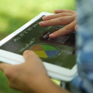 A child outside holding a tablet with an overlay. They are exploring the overlay with their finger.