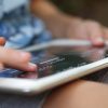 A child outside holding a tablet with an overlay. They are exploring the overlay with their finger.
