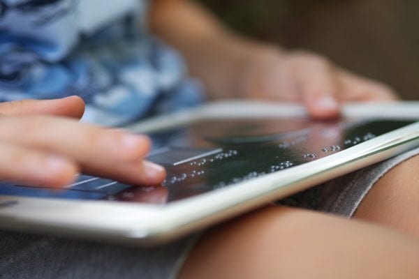 A child outside holding a tablet with an overlay. They are exploring the overlay with their finger.